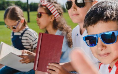 Symbolbild: Vier lesende Kinder mit Sonnenbrillen
